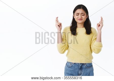 Wishful Tensed Young Cute Asian Girl Cross Fingers For Good Luck, Pursing Lips And Close Eyes As Ple