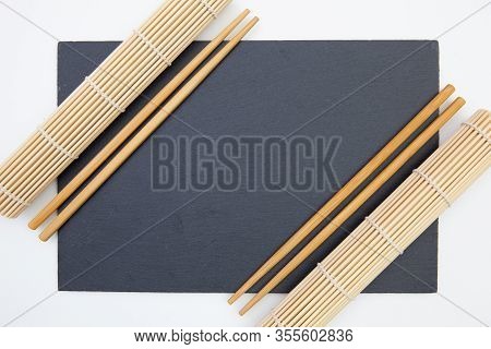 Rectangular Slate Plate With Chopsticks, Bamboo Mat  For Sushi On The White Table. Food Design