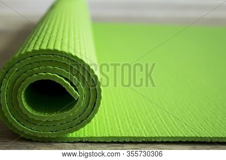 The Yoga Mat Of Green Color Lies On The Floor. Healthy Lifestyle. Light Background, Blur Of The Back