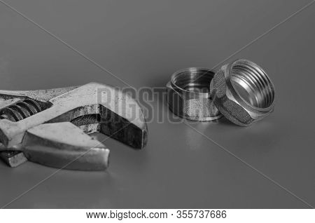 Adjustable Wrench And Two Nuts On A Drey Background. Repair And Installation Of Water Supply. Select