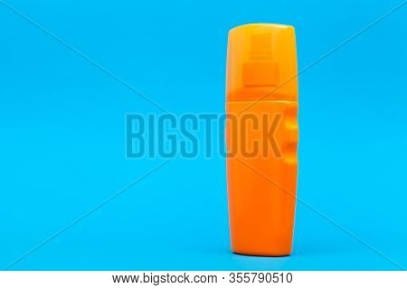 Orange Plastic Bottle Of Suntan Cream Side View On A Blue Background With Copy Space.