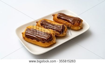 Plate Custard Cakes With Chocolate Icing On A White Background. Copy Space