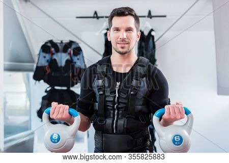 Strong man in ems gym doing fitness training with weights looking at the camera