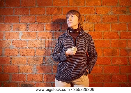 A Middle-aged Woman Poses Showing Clothes Near Red Brick Wall. An Inept Model In An Inept Shoot