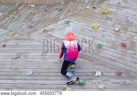 The Child In A Bright Pink Jacket Is Climbing A Wooden Wall