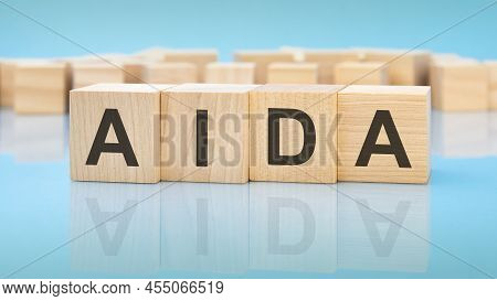 Word Aida On Wooden Cubes On Blue Background. The Inscription On The Cubes Is Reflected From The Sur