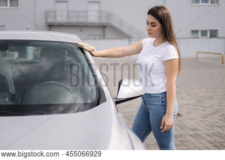 Front View Of Attractive Happy Joyful Female Driver Washing Her Cars Headlights With Special Rag In 