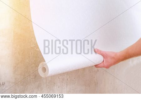 A Man Rolls Out A Roll Of White Wallpaper On The Wall With Glue. Wallpapering. Repair Of A Room, Apa