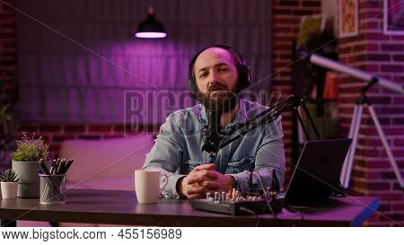 Portrait Of Man Recording Podcast Using Audio Mixer And Laptop Computer Talking In Professional Micr