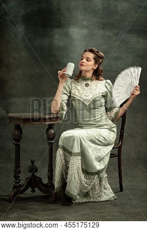Vintage Portrait Of Young Beautiful Girl In Gray Dress Of Medieval Style Drinking Tea Isolated On Da