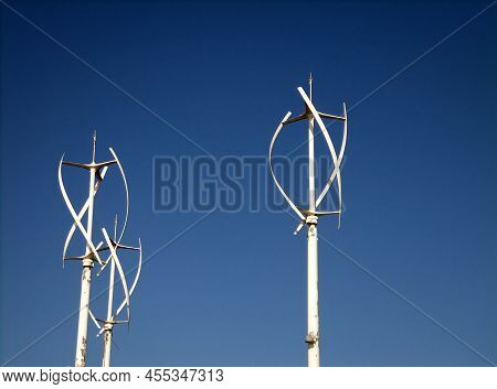 A Group Of Small Vertical Wind Turbines Against A Blue Sky