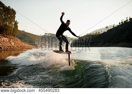 Athletic Man Skillfully Balances On Splashing Wave On A Foil Wakeboard