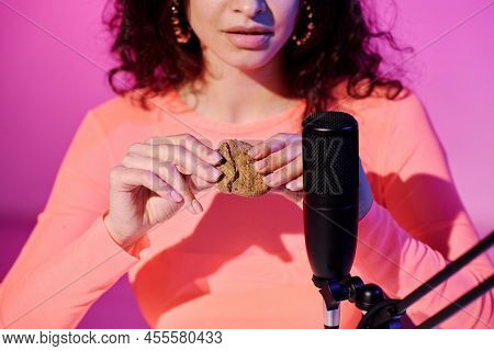 Young Female Blogger Sitting In Studio In Pink Neon Light Recording Crunchy Cookies Breaking Sound F