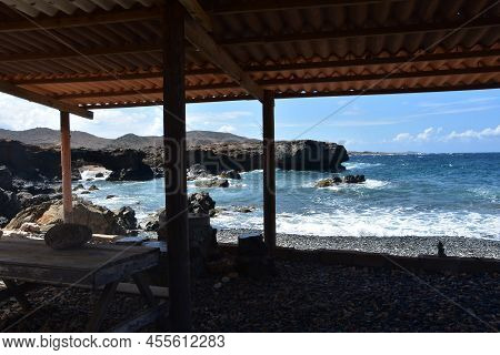 Structure Creating Shade Along The Coast Of A Black Stone Beach In Aruba.