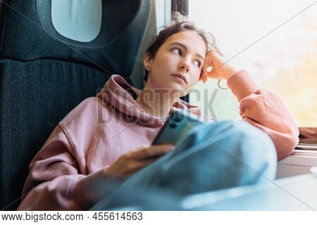 Pensive Lonely Teenage Girl Sits In Train Near Window, Resting  Head On Hand, Looking Out Window, Ho