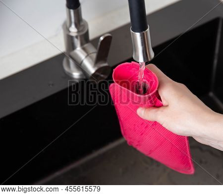 A Woman Pours Hot Water Into A Medical Heating Pad From The Tap. Treatment Of Diseases With Heat, Cl