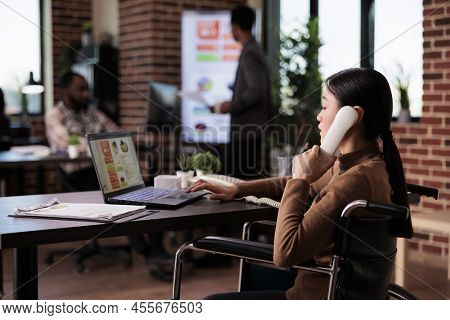 Female Employee With Health Condition Answering Landline Phone Call In Disability Friendly Office. U