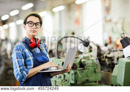 Serious Smart Young Woman With Ear Protectors On Neck Standing In Industrial Shop Of Watch Factory A
