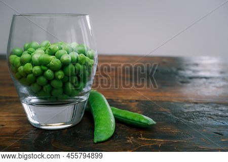 Green Peas In Glass Bowl. Fresh Pea In The Pod With Green Leaves. Green Peas On A Brown Wodden Table