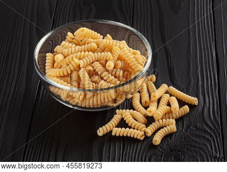 Uncooked Fusilli Pasta In Glass Bowl On Black Wooden Background
