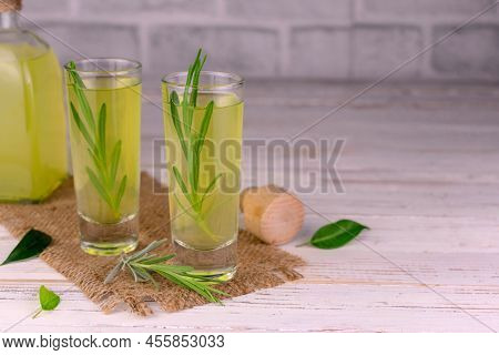 Limoncella With A Sprig Of Rosemary. Italian Lemon Liqueur On A White Wooden Background.copy Space.