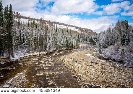 The Not Frozen Bed Of A Beautiful Winding Chibit River Flowing Through A Snow-covered Valley Surroun