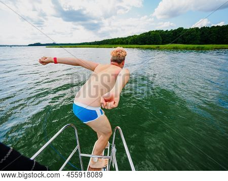 Young Man Jumping From A Sailing Yacht Deck Into A Lake, View From Back