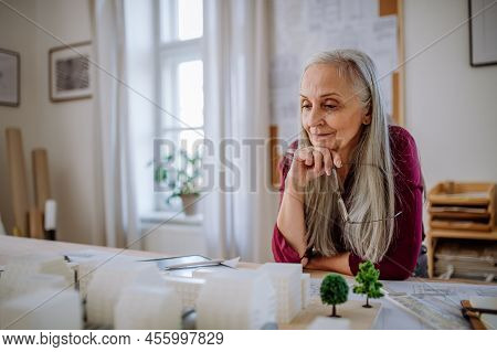 Senior Woman Eco Architect With Model Of Modern Bulidings Working In Office.