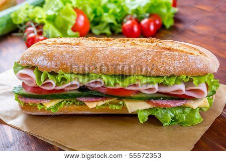 Long Baguette Sandwich with lettuce, slices of fresh tomatoes, ham, turkey breast and cheese