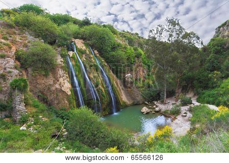 Three parallel streams of water running down the steep slope and fall in oval pool. Unusual three-jet waterfall in northern Israel