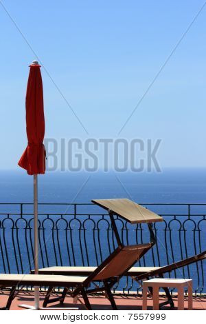 Red Umbrella And Sunbeds Overlooking The Mediterrean Sea