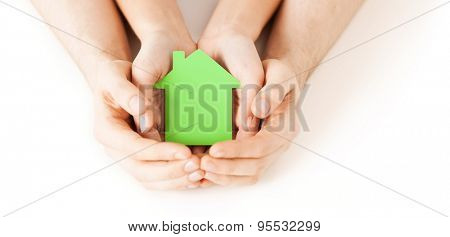 real estate and family home concept - closeup picture of male and female hands holding green blank paper house