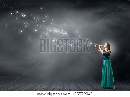 Young pretty woman in green long gress playing fife