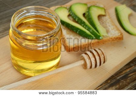 Golden honey with honeystick and a healthy sandwich with green avocado on wooden board