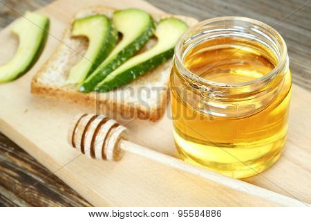 Golden honey with honeystick and a healthy sandwich with green avocado on wooden board