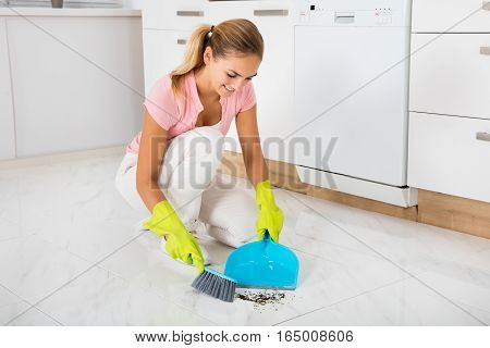 Smiling Woman Sweeping Floor With Broom And Dustpan In The Kitchen