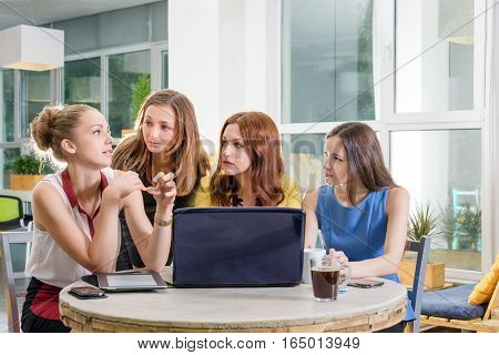 Group of four pretty businesswomen working togeather with new startup project using laptop computer in modern loft. People and teamwork concept - happy creative team in office. Casually dressed female colleagues talking in a meeting room.