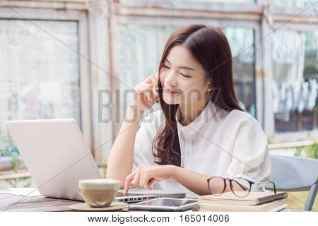 young happy casual asian woman using technology on her laptop computer and her phone