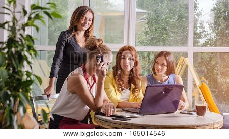 Group of four pretty businesswomen working togeather with new startup project using laptop computer in modern loft. People and teamwork concept - happy creative team in office. Casually dressed female colleagues talking in a meeting room.