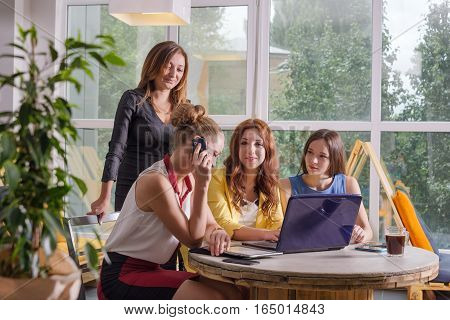 Group of four pretty businesswomen working togeather with new startup project using laptop computer in modern loft. People and teamwork concept - happy creative team in office. Casually dressed female colleagues talking in a meeting room.