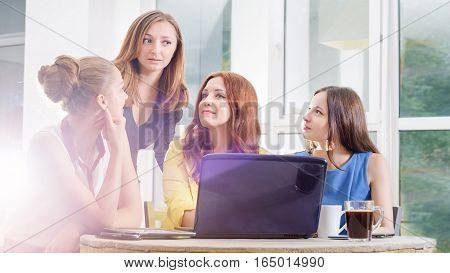 Group of four pretty businesswomen working togeather with new startup project using laptop computer in modern loft. People and teamwork concept - happy creative team in office. Casually dressed female colleagues talking in a meeting room.