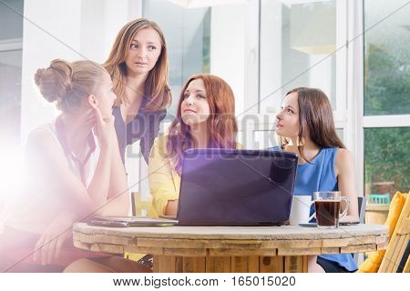 Group of four pretty businesswomen working togeather with new startup project using laptop computer in modern loft. People and teamwork concept - happy creative team in office. Casually dressed female colleagues talking in a meeting room.