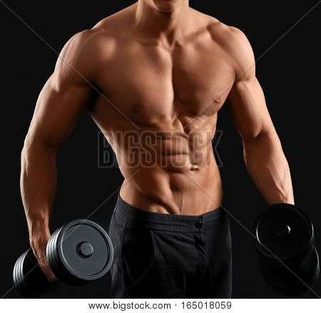 Body of God. Cropped shot of a strong and muscular male bodybuilder holding dumbbells against black background