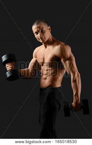 How workout is done. Happy male bodybuilder exercising with dumbbells smiling to the camera on black background