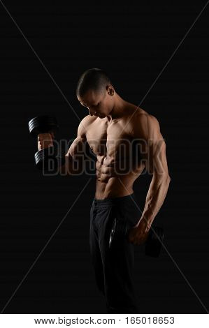 Devoted sportsman. Vertical shot of a hot and sexy shirtless muscular man posing on black background with dumbbells in his hands