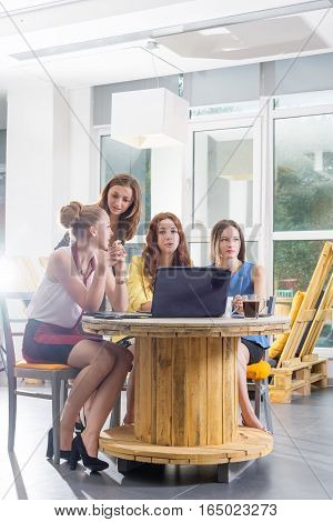 Group of four pretty businesswomen working togeather with new startup project using laptop computer in modern loft. People and teamwork concept - happy creative team in office. Casually dressed female colleagues talking in a meeting room.