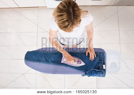 High Angle View Of Young Woman Ironing Jeans On Ironing Board At Home