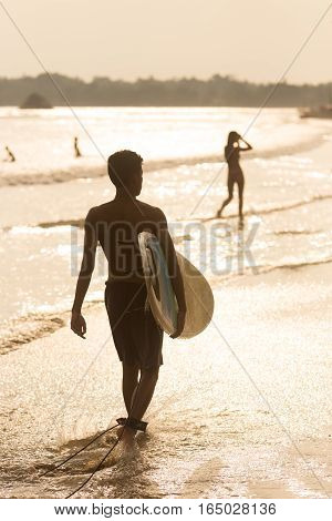 Silhouette of male surfer on the beach with the surfboard in sunset.