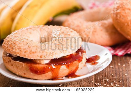 Sesame bagels with jam and bananas on white dish.