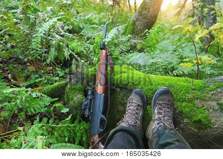 Hunter in the autumn forest with a rifle at sunrise. Legs and the carbine on foreground.